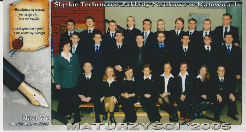 Kolorowe zdjęcie Maturzystów ‘2005 klasa Vc rok szkolny 2004/2005, u góry napis Śląskie Techniczne Zakłady Naukowe w Katowicach; maturzyści w trzech rzędach: pierwszy siedzi na ławeczce (w środku 6 dziewcząt, po bokach chłopcy), drugi i trzeci rząd chłopców stoi, wszyscy w mundurkach z tarczami; z lewej strony wychowawczyni klasy, tło hol szkolny