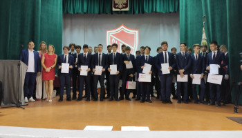 Zdjęcie grupowe uczniów z certyfikatami, w tle zielone kotary, godło i tarcza szkoły