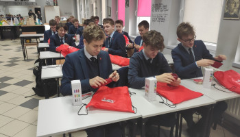 Uczniowie z czerwonymi workami z napisem Fujitsu-P-Tech oglądający otrzymane gadżety