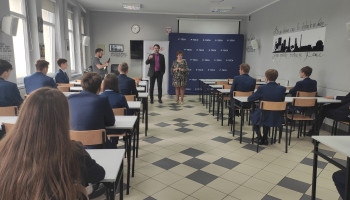 Uczniowie w sali lekcyjnej słuchający mówiącego mężczyzny