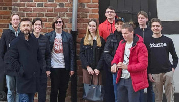 Zdjęcie grupowe uczniów z opiekunem, w tle mur z czerwonej cegły