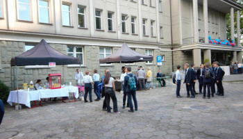 plac przed szkołą, pod murem budynku stoiska z napojami, watą cukrową; grupki uczniów, nauczycieli podczas festynu