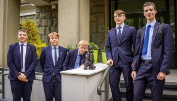 5 uczniów w garniturach w trakcie pamiątkowego zdjęcia z bebokiem „Ancugiem”