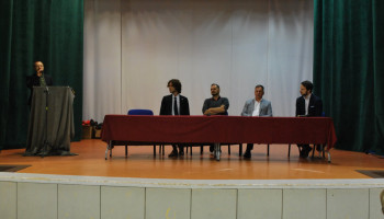 przemowa prowadzącego debatę (przy mównicy), na scenie za stołem prezydialnym uczestnicy (4 osoby)